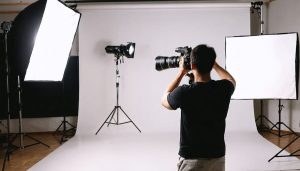 A photographer adjusting indoor lighting equipment like softboxes and reflectors in a room used as a makeshift studio, demonstrating professional lighting techniques.