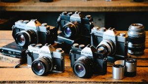 A collection of vintage film cameras displayed on a wooden table, accompanied by rolls of film, showcasing the variety and charm of analog photography equipment.