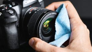 Photographer carefully cleaning a camera lens with a premium microfiber cloth, illustrating the cloth's fine structure and precision in maintaining lens clarity.