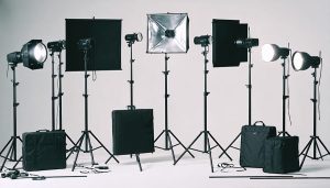 A well-organized studio photography setup displaying different types of lighting equipment, including strobes, continuous lights, and LED panels, with visible interplay of light and shadows.