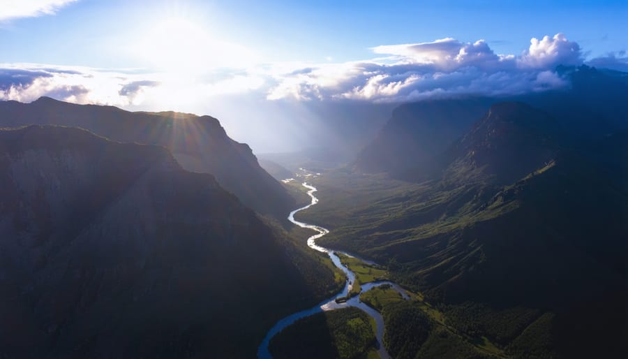 Aerial view from a drone showcasing a sunrise over a mountain range, with a winding river and ridgelines creating leading lines toward the horizon, and low-hanging clouds adding depth.