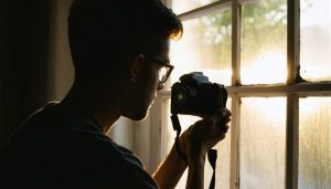 A photographer capturing a portrait by a large window, demonstrating the use of natural light to create soft, flattering shadows on the subject.