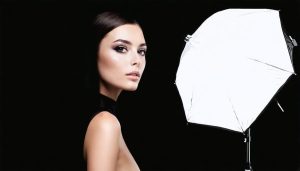 A professional studio setup showcasing various lighting modifiers including a beauty dish, softbox, and umbrella positioned around a model, demonstrating the transformative effect of these tools on photographic lighting.