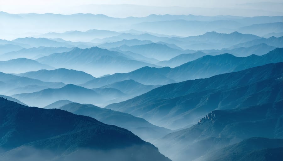 A telephoto lens captures layered mountain ranges, with atmospheric mist enhancing the depth and ethereal quality. The compression effect emphasizes the landscape's intricate patterns and scale, creating a dramatic and artistic composition.